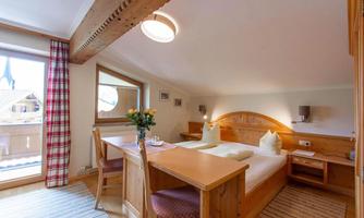 A cozy bedroom with wooden details and two beds. A small table with a flower vase complements the inviting atmosphere.