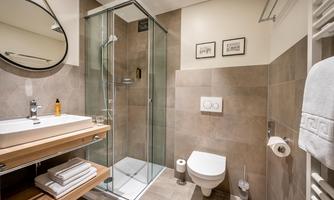 A modern bathroom with a glass shower and a sink on wooden shelves. The walls are painted in neutral tones, and there are some decorative pictures displayed.