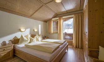 A cozy bedroom with two single beds and wooden paneling. Large windows let in plenty of daylight and offer a view outside.