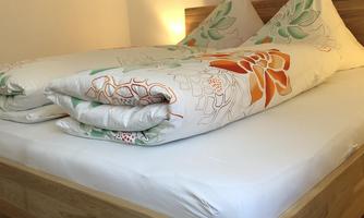 A cozy bed with colorful cushions and blankets. The wooden floor adds a warm atmosphere to the room.