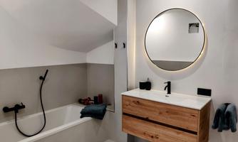 A modern bathroom with a bathtub and a simple wooden washbasin. A round mirror illuminates the space and creates a pleasant atmosphere.