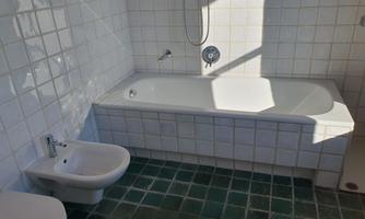 A bathroom with a bathtub and a bidet and toilet. The walls are tiled and the floor has green tiles.