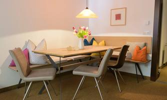 A modern dining area with a large wooden table and stylish chairs. Vases with flowers and colorful cushions create a cozy atmosphere.