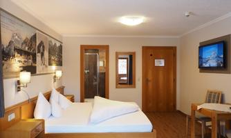 A cozy hotel room with a double bed and wooden furniture. The walls are decorated with pictures, and there is a television as well as a small table.