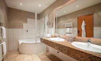 A modern bathroom with a bathtub and a shower. The room is bright and elegant, with two sinks and large mirrors.