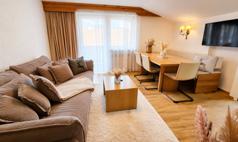 A cozy living room with an inviting sofa and a wooden table.  
Large windows let in plenty of light and provide a pleasant atmosphere.