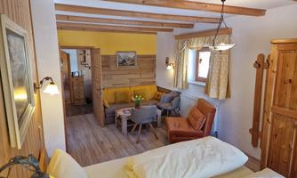 A cozy room with a wooden ceiling, a double bed, and a seating area. The room is bright and friendly with a warm color selection.