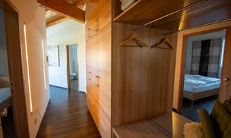 A bright hallway with wooden details and an open wardrobe. In the background, two bathrooms and a bedroom are visible.