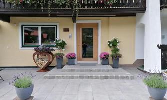 An inviting entrance area with a wooden portal and blooming plants. Flowers in pots and a heart-shaped decoration add a lovely charm to the ambiance.