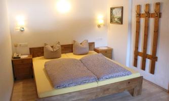 A cozy bedroom with a large double bed and wooden dressers. On the wall hangs a picture and a wooden coat rack.