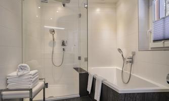 A modern bathroom with a shower and a bathtub. Fresh towels are ready on a chair.