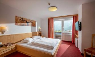 A cozy bedroom with a double bed and a large window. The walls are light, and the decor is simple and inviting.