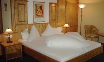 A cozy bedroom with a double bed and decorative cushions. There are wooden paneling, nightstands, and a relaxed seating area.