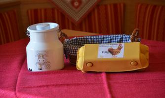 A white pitcher with a cow motif stands next to a yellow basket, which is lined with a checked cloth. The basket has a label that reads "Bobergeris."