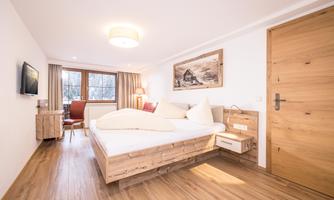 A modern bedroom with a large wooden bed and elegant furnishings. Large windows let in plenty of natural light.