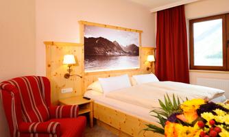 A cozy hotel room with a double bed and a red armchair. A picture of a mountain landscape hangs on the wall and there are fresh flowers on the table.