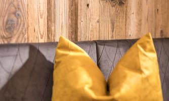 A cozy seating area with a gray couch and two bright yellow pillows. The wall is made of warm, planed wood.