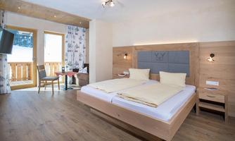 A modern furnished bedroom with a double bed and wooden floor. Large windows offer a view of a balcony overlooking the outdoors.