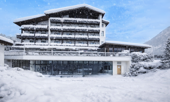A modern hotel building in a snow-covered winter landscape. The sky is blue and it is lightly snowing.