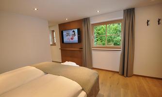 A modern bedroom with a double bed and a TV on the wall. The window offers a view outside and the decor is bright and designed in a minimalist style.