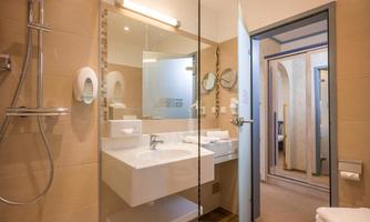 A modern bathroom with a glass shower enclosure, a sink, and large mirrors. The walls are in warm beige tones.