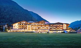 A beautiful hotel in the mountains, illuminated at twilight. Surrounded by lush greenery and majestic mountains.
