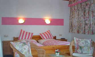 A cozy bedroom with a double bed and striped pillows. Two basket chairs and a small table create an inviting atmosphere.