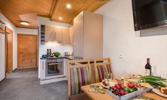 A cozy kitchen with wooden ceilings and modern appliances. The table is festively set with an assortment of fresh fruit and wine.