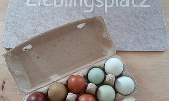 A box with several colorful eggs is on a table. Next to it is the inscription "Favorite Place" on a placemat.
