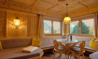 A cozy dining area with wooden paneling and large windows that offer views of the mountains. The table is beautifully set and surrounded by modern chairs.