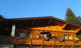 A beautiful wooden house with a balcony and blooming flowers. The clear sky and the trees in the background create a cozy atmosphere.