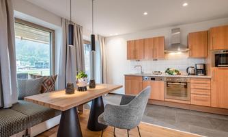 A modern kitchen with wooden cabinets and a large dining table. The windows offer a lovely view outside and let in plenty of light.