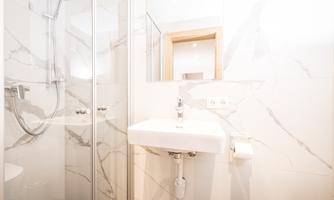 A modern bathroom with a sink and a glass shower. The walls are decorated with elegant marble tiles.