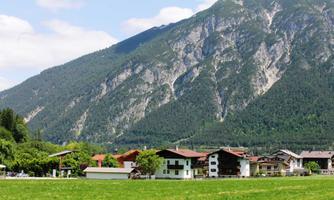 A picturesque landscape with a large mountain in the background. In the foreground, you can see peaceful meadows and several traditional houses.