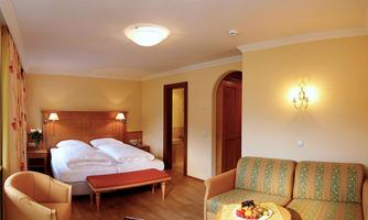 A bright hotel room with a double bed and a cozy sofa. There is a fruit bowl on the table.