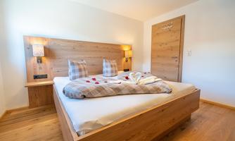A cozy bedroom with a wooden loft bed and modern lamps. The bed is lovingly decorated with a blanket and towels in heart shape.
