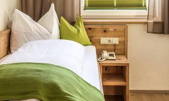 A cozy bedroom with a single bed and green pillows. Next to the bed is a bedside table with a telephone.