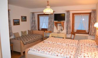 A cozy bedroom with two beds and an additional sleeping place. Large windows ensure ample daylight.