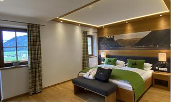 A modern bedroom with a large bed and elegant wooden ceiling. The windows offer a view of a beautiful mountain landscape.