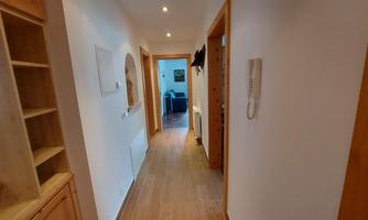 A bright hallway with wooden floors and warm walls. At the end of the hallway, a cozy living space is visible.