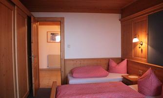 A cozy room with two beds and checked pillows. The walls are made of wood, and there is a door to another room.