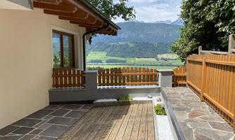 A cozy terrace with wood decking and stone tiles. In the background, there is a beautiful view of the mountains and the valley.