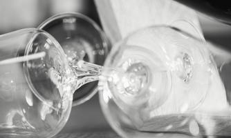 Two tipped-over glasses are lying on a table. In the background, a blurred note is visible.