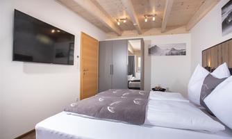 A modern bedroom with a large bed and wooden ceiling. On the wall, there is a television and some beautiful photos.