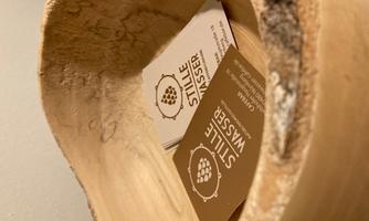 A wooden bowl containing two business cards. The cards are labeled with "STILLE WASSER".