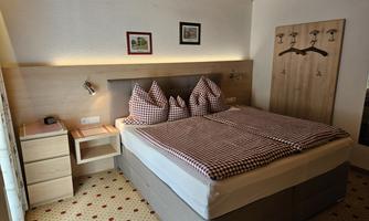 A cozy bedroom with a large bed and checkered pillows. The walls are light and there is a wooden ceiling that creates a warm atmosphere.