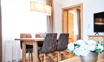 A modern dining area with a wooden table and stylish chairs. Bright light streams through the windows, creating an inviting atmosphere.