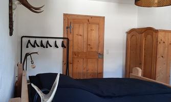 A cozy bedroom with a wooden bed and a black bed cover. Antlers hang on the wall and there is a wooden wardrobe as well as a lamp with a modern design.