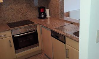 A modern kitchen with wooden cabinets and a granite countertop. It includes a stove, a dishwasher, and a coffee machine.