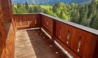 A beautiful wooden balcony with a view of the mountains. The landscape is green and interspersed with clouds.